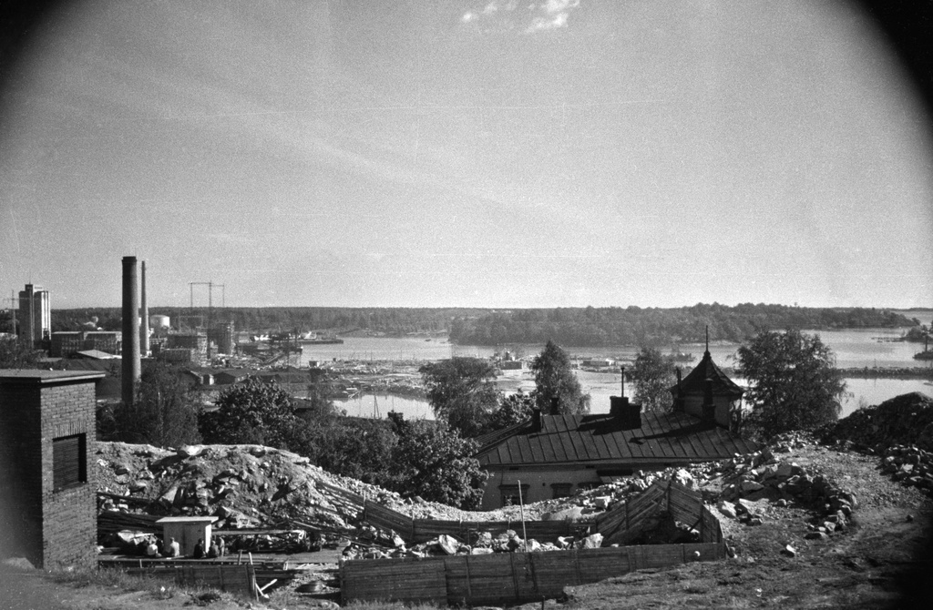 Näkymä Sörnäisten rantatie 25 kohdalta. Edessä rakennustyömaa ja puuhuvila. Kauempana puiden peittämä Sompasaari ja lähempänä Hanasaari.