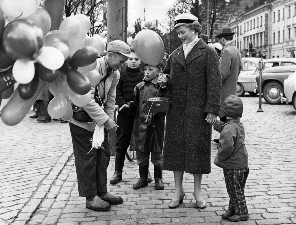 Elanto-lehti 3/9/58. Vappu. Nainen, jolla on ylioppilaslakki päässään ostamassa ilmapalloja lapsilleen Esplandin puiston vieressä, kauppatorin laidalla.