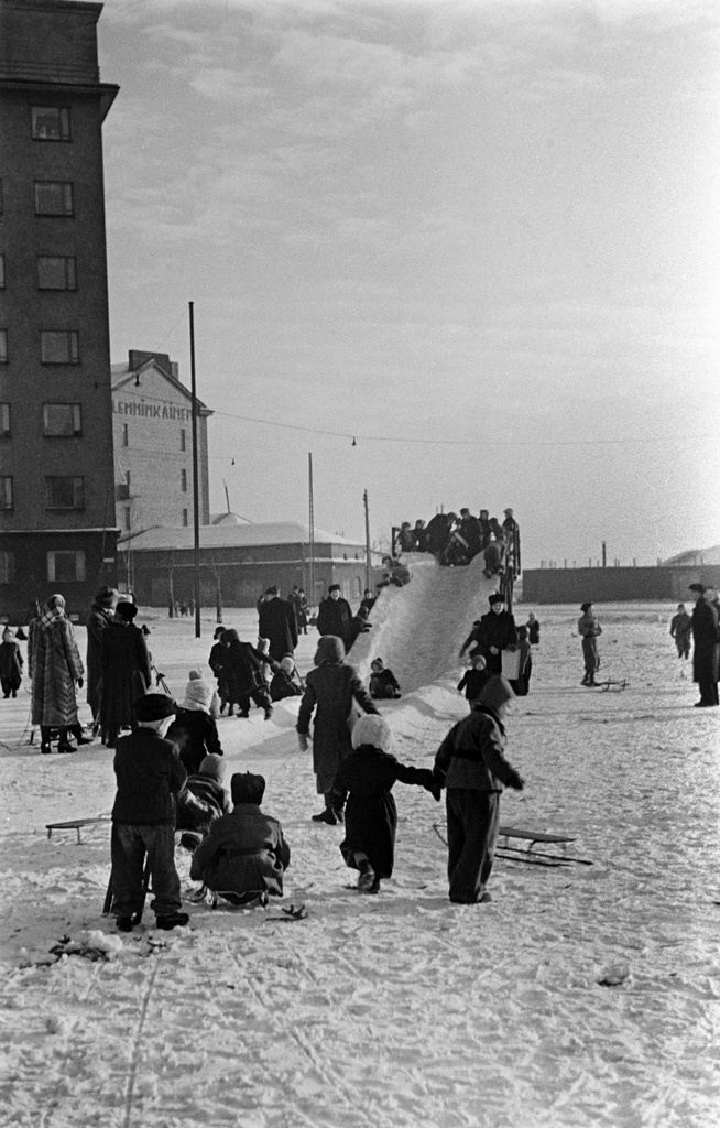 Jäämäki ja lapsia laskemassa mäkeä Hakaniementorin kaakkoiskulmassa. Taustalla Viherniemenkatu 1 ja Hakaniemenkatu 2.