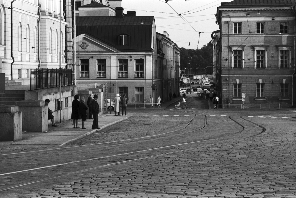 Snellmaninkatu 1. Aleksanterinkatu 18, 20. Näkymä Snellmaninkadulta Hallituskadun kulmasta Katariinankadun suuntaan. Vasemmalla ihmisiä pysäkillä Valtioneuvoston linnan edessä. Taustalla Aleksanterinkadun kulmassa vasemmalla Sederholmin talo, oikealla Bockin talo.