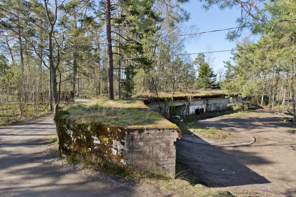 Skatanniemi. Ensimmäisen maailmansodan aikainen rannikkotykkipatteri Skatanniemessä, Vuosaaressa. Kuvassa on rintasuoja, jonka taakse on sijoitettu yhteensä neljä tykkiasemaa. Betonista valmistetun rintasuojan seinässä näkyy ampumatarvikekomero. Seinällä erottuu myös kaksi pientä ikkunaa, joista näkee sisälle rintasuojan alle rakennettuihin miehistö- ja varastotiloihin. Keskellä on betonista valettu jalusta itse tykille, jota ei koskaan saatu paikalle. Jalustan keskellä oleva pulttirinki kertoo mihin tykki oli tarkoitus kiinnittää. Vasemmalla kulkee tie, joka on puhkaistu asemaan 1920-luvulla. Kuvaussuuntana lounas.
