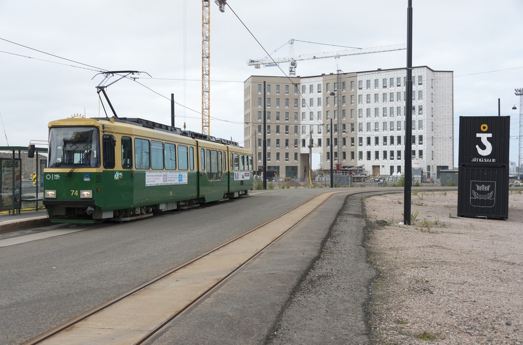 Jätkäsaaren dokumentointi. Raitiovaunu 8 päätepysäkki, taustalla Atlantinkatu 7. Oikealla musta kontti, jossa Jätkäsaaren logo (nosturin koukku), Helsingin vaakuna ja teksti: "Jätkäsaari".