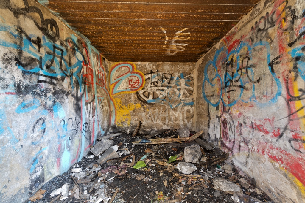 Länsimäki. Ensimmäisen maailmansodan aikainen maalinnoitus, puolustusasema II:7, kaakkoinen puolustusasema C Länsimäessä, Vantaalla. Kuvassa on kaksihuoneisen suojahuoneen toinen huone. Rakenteet on tehty betonista. Sisäkaton teräspalkit on jätetty paikoilleen. Seinät ovat graffitien peitossa. Myös katon palkkeihin on spreijattu. Pohja on erilaisten jätteiden ja roskien vallassa. Kuvaussuuntana koillinen.