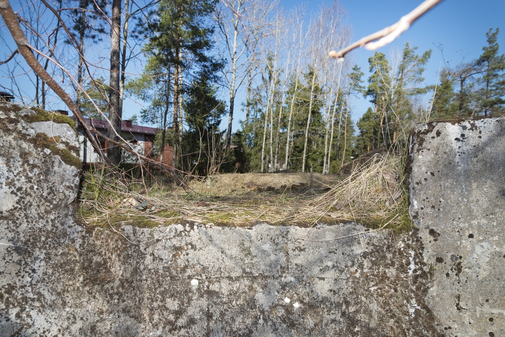 Länsimäki. Ensimmäisen maailmansodan aikainen maalinnoitus, puolustusasema II:7, pohjoinen puolustusasema A Länsimäessä, Vantaalla. Kuvassa on kallioon louhittu, betonilla tuettu konekivääriasema ja sen ampuma-aukko. Aukko avautuu levenevään reunoiltaan porrastettuun ampumasektoriin. Taustalla näkyy puita ja asuinrakennuksia. Kuvaussuuntana luode.