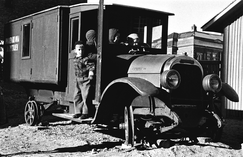 Elannon päiväkodin lapsia leikkimässä Viides linja 4:n pihalla olevan vanhan auton luona. Auto on käytöstä poistettu leipäauto ja siitä on tehty lasten leikkipaikka. Sen kyljessä lukee "poikien ikioma ja tyttöjen". Taustalla Kallion kirjasto.