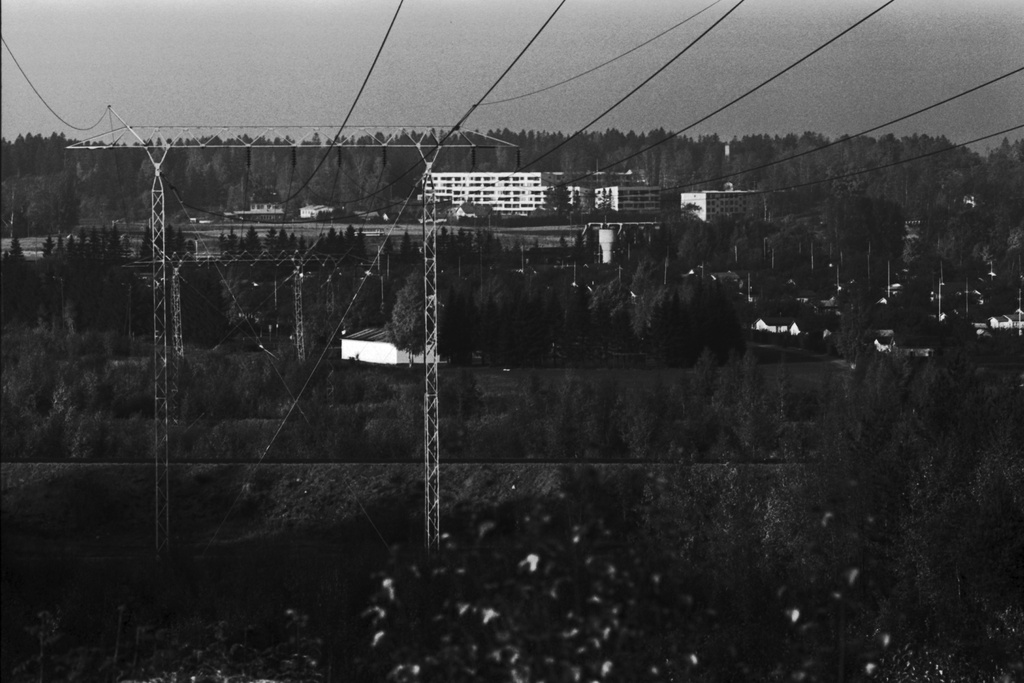 Näkymä Pirunkalliolta pohjoiseen Oulunkylän Veräjämäessä. Keskellä voimajohtolinja, oikealla Oulunkylän siirtolapuutarhan mökkejä. Taustalla kerrostaloja.