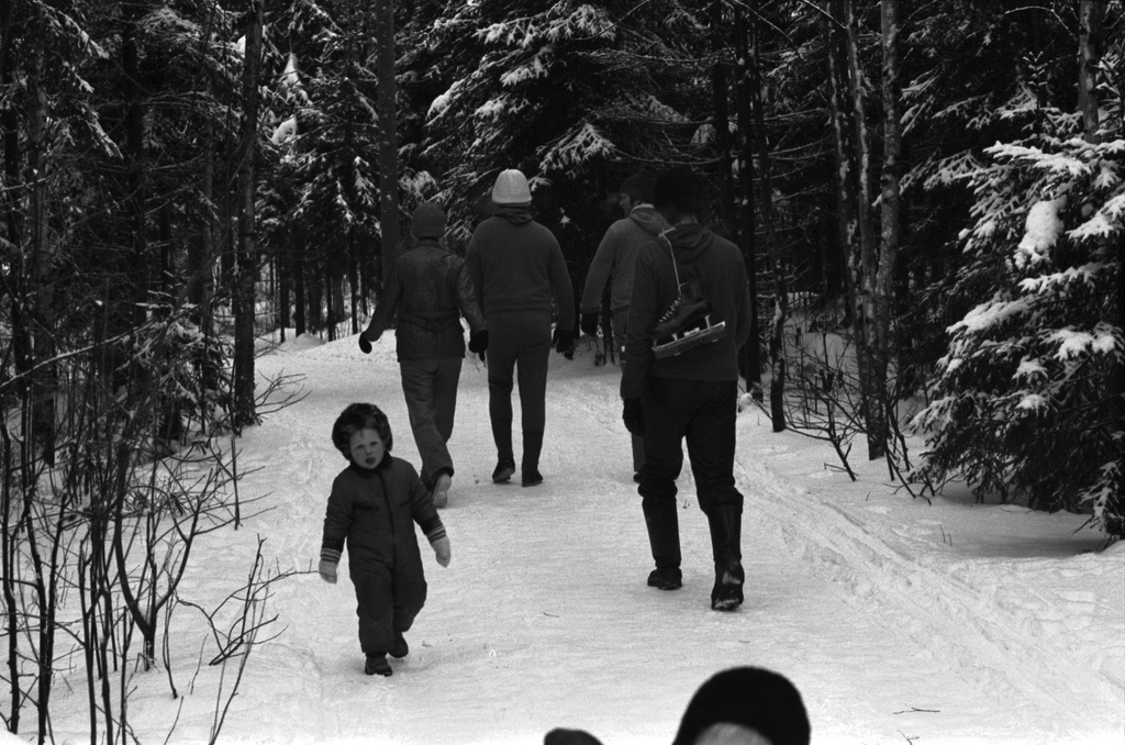 Pirkkolan urheilupuisto. Ihmisiä ulkoilemassa talvisessa Pirkkolan urheilupuistossa. Keskellä kävelelee mies hokkarit olalla.