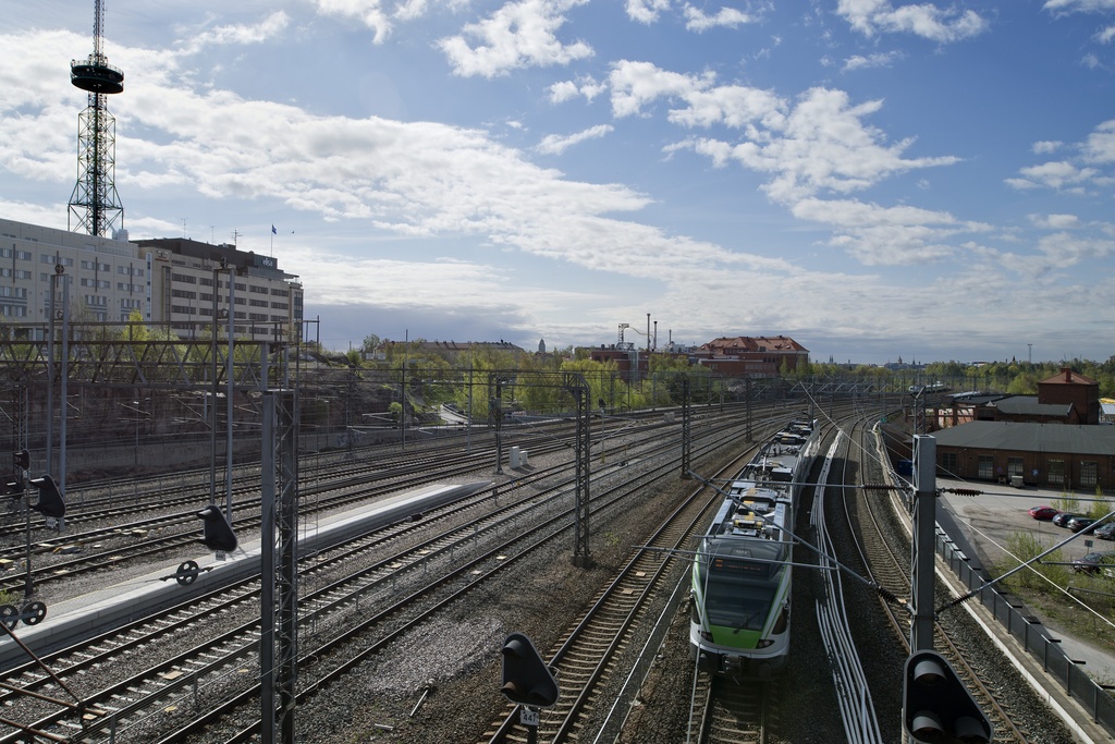 Pasilan asema. Rautatiet Pasilan asema-aukiolta etelään kuvattuna. Vasemmalla Elisan radiomasto, keskellä Stadin ammattiopisto ja Eläintarhan koulu ja oikealla entiset VR:n varikkorakennukset. Taustalla häämöttää Linnanmäki.