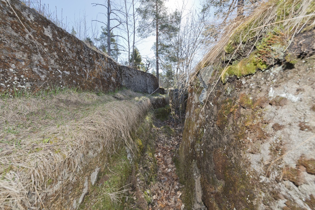 Länsimäki. Ensimmäisen maailmansodan aikainen maalinnoitus, puolustusasema II:8 Länsimäessä, Vantaalla. Kuvassa näkyy kallioon louhittua, betonilla tuettua louvasti mutkittelevaa taisteluhautaa aseman koillisosassa. Rintasuojan alaosassa on torjuntasuunnan puolella ampumakoroke sekä kapea porras helpottamaan nousua tälle ampumakorokkeelle. Kuvaussuuntana itä.