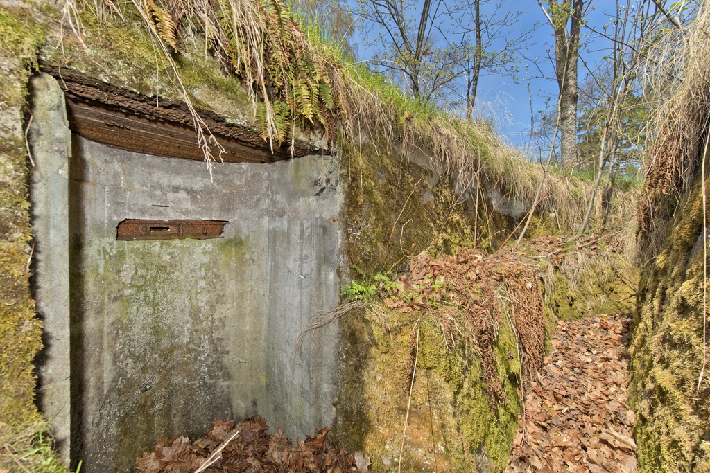 Haukilahti. Ensimmäisen maailmansodan aikainen maalinnoitus, puolustusasema XXXIV:13 Haukilahdessa, Espoossa. Kuvassa on kallioon louhittua, betonilla tuettua taisteluhautaa sekä rintasuojaan tehty syvennyksenomainen tähystysasema. Aseman etuseinä on muodoltaan kaareva. Katon teräksiset tuet on jätetty paikoilleen. Seinässä on tähystysaukko, joka on voitu sulkea metalliluukulla. Aseman oikealla puolella jatkuvan haudan rintasuojan alaosassa on torjuntasuunnan puolella ampumakoroke.