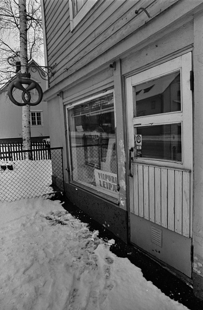 Viipurin Leipä Oy:n leipomon myymälä puurakennuksessa Toukolassa. Myymälän näyteikkuna ja sisäänkäynti. Rakennuksen ulkoseinässä on viipurinrinkelin muotoinen mainoskyltti.