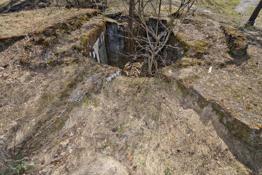 Länsimäki. Ensimmäisen maailmansodan aikainen maalinnoitus, puolustusasema II:7, pohjoinen puolustusasema A Länsimäessä, Vantaalla. Kuvassa on kallioon louhittu betoninen konekivääriasema aseman länsilaidalla. Asema on päämuodoltaan neliömäinen, mutta ampuma-aukon puoleinen sisäseinä on kaareva. Ampumasektoria reunat on porrastettu. Vasemmalla seinällä näkyy konekiväärin jäähdytysvesisäiliötä varten tehty komero. Oikealla seinällä on pienempi komero, jonka tarkoitusta ei tiedetä. Takaseinän sisäänkäynti avautuu taisteluhautaan. Aseman kattamistyöt ovat mahdollisesti jääneet keskeneräisiksi. Pohjalla on betoninpaloja. Aseman sisällä kasvaa nuoria puita.Kuvaussuuntana itä-kaakko.