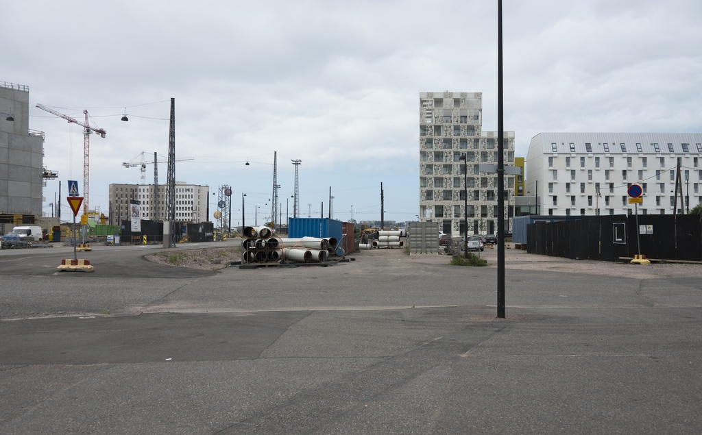 Jätkäsaaren dokumentointi. Länsisatamankatu 23 j 21, taustalla Atlantinkatu 7. Etualalla tilapäinen aukio, jossa kontteja, rakennusmateriaaleja ja työmaa-aitaa.