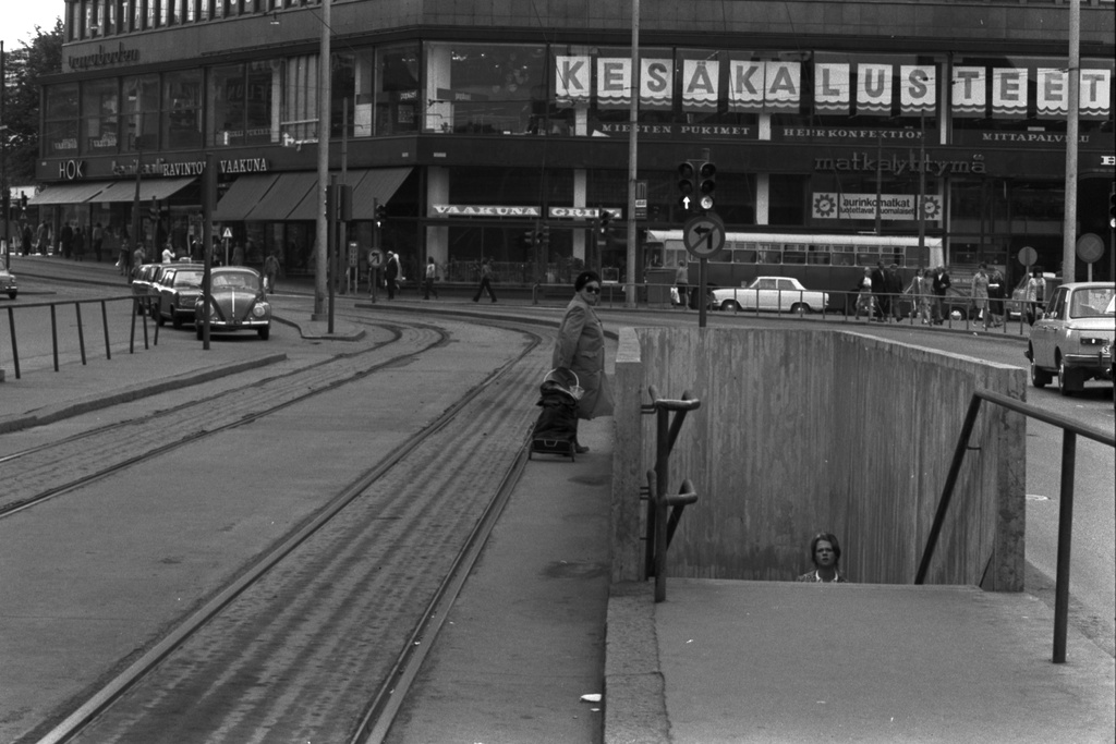 Kaivokatu. Nainen ylittämässä Kaivokatua liikennesääntöjen vastaisesti raitiotiekiskoja pitkin Asematunneliin johtavan betonisen alikulkutunnelin vierestä.