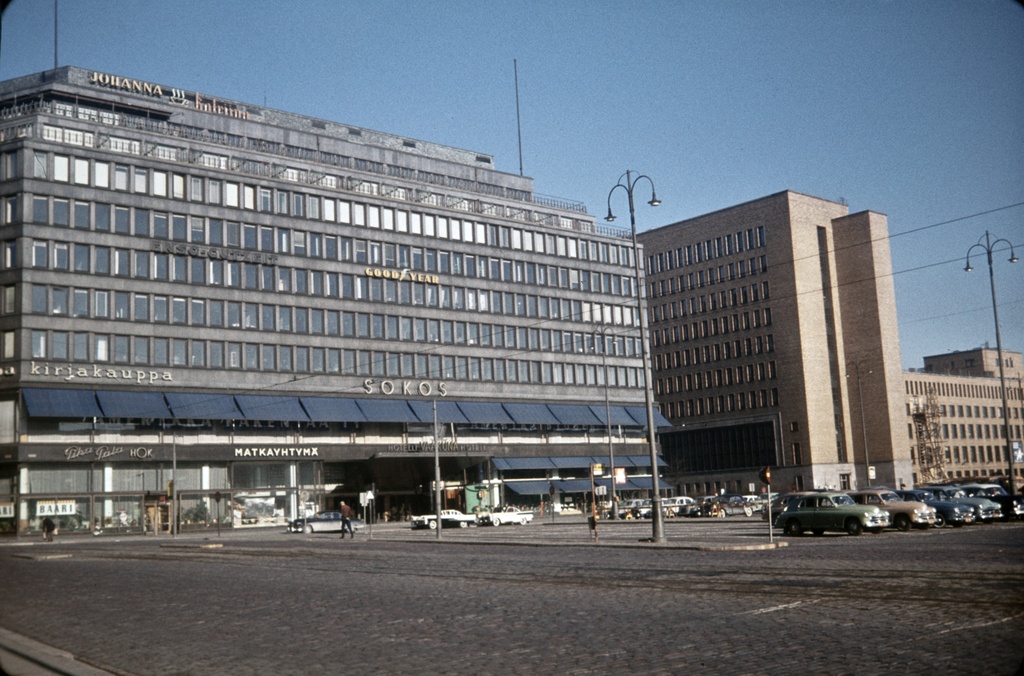 Asema-aukio 2, 5. Sokos-tavaratalo, Postitalo. Sokoksen seinässä valomainoksia: Johanna, Katriina (kahveja), Enso-Gutzeit, Goodyear, kirjakauppa, Sokos, Pika-Pala HOK, Matkayhtymä, Hotelli Vaakuna. Katutasossa baari.