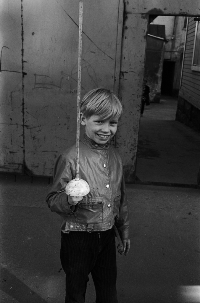 Neljäs linja 6, 8. Hymyilevä poika miekka kädessä kadulla Neljäs linja 6:n pihalle vievän portin edessä.