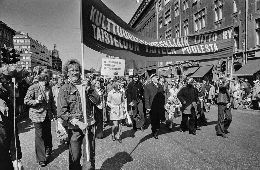 Vappumarssijoita Mannerheimintiellä Stockmannin tavaratalon kohdalla. Kaksi miestä kantaa Kulttuurityöntekijäin liiton banderollia. Yleisö seuraa marssia kadun varrella.