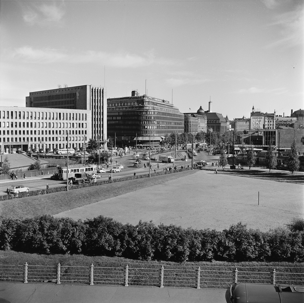 Mannerheimintie nähtynä Eduskuntatalolta kohti Postitaloa, Mannerheimintie 11 (= Mannerheiminaukio 1), ja Sokosta, Mannerheimintie 9. Etualalla nimetön puisto ja kenttä (= Pikkuparlamentin puisto).