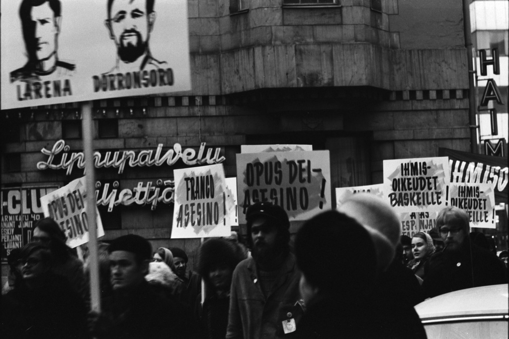 Kluuvi, Mannerheimintie 5. "Ihmisoikeudet baskeille, alas Espanjan fasismi" -mielenosoituskulkue lähtenyt liikkeelle Uuden ja Vanhan ylioppilastalon väliseltä aukiolta, ns. Perunatorilta. Plakaateissa mm. tekstejä: Franco asesino! Opus Dei - asesino! Ihmisoikeudet baskeille! Taustalla Lippupalvelun neonvalokyltti.