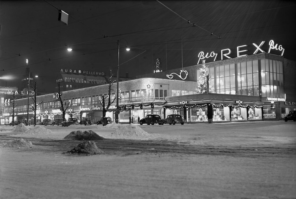 Lasipalatsi, Heikinkatu 28 (Mannerheimintie 22-24) iltavalaistuksessa. Etualalla Bio Rex ja HOK. Joulukoristelua. Rakennuksen piirtäneet Kokko, Revell ja Riihimäki, valmistunut 1936.