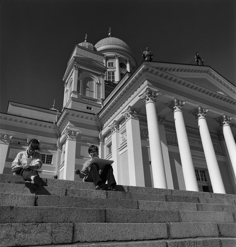 Nainen ja mies istuvat Tuomiokirkon portailla. Taustalla Tuomiokirkko.