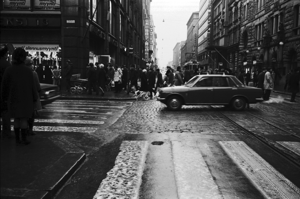 Kluuvi, Aleksanterinkatu. Aleksanterinkadun kävelykatukokeilu (12.6.1970-8.1.1971) on päättynyt. Jalankulkijoita ja ajoneuvoliikennettä Aleksanterinkadun ja Mikonkadun kulmassa puolen päivän aikaan. Näkymä Senaatintorin suuntaan.