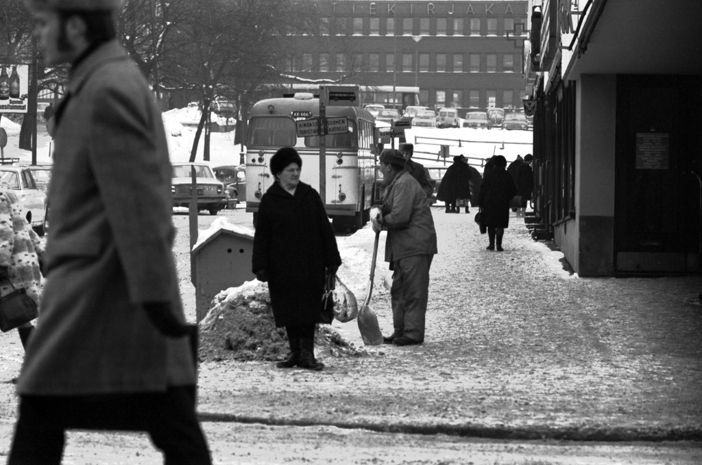 Jalankulkijoita ja lapioon nojaava mies Lasipalatsin kulmalla. Näkymä Mannerheimintiellä Simonkentän suuntaan. Taustalla Annankatu. Talvi, lunta maassa.