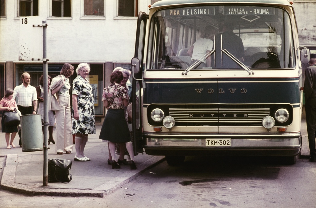 Linja-autoja ja matkustajia linja-autoaseman lähtölaitureilla, taustalla Lasipalatsin myymälöitä.