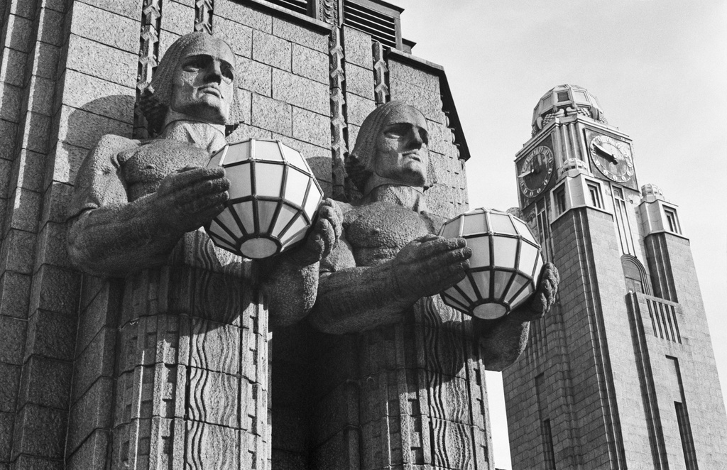 Kaivokatu 1. Kuvanveistäjä Emil Wikströmin veistämät graniittiset Lyhdynkantajat-hahmot Helsingin rautatieaseman pääsisäänkäynnin oikealla puolella. Taustalla aseman kellotorni.