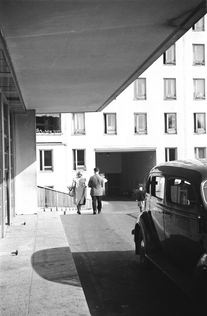 Naistenklinikka, Haartmaninkatu 2. Naistenklinikan pihanpuoleisen oven rampilla auto sekä ramppia alas kävelevät mies ja nainen.