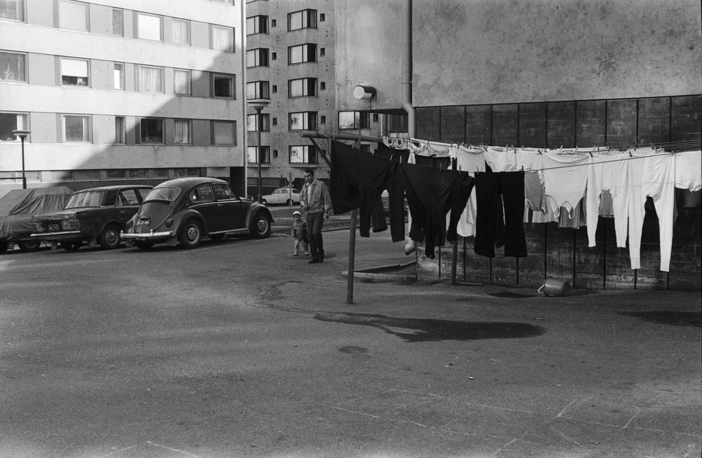 Neljäs linja 17, 19. Neljäs linja 17-19:n pihapiiriä, jossa pyykkiä kuivumassa narulla, mies ja lapsi sekä pysäköityjä autoja. Taustalla Neljäs linja 22.