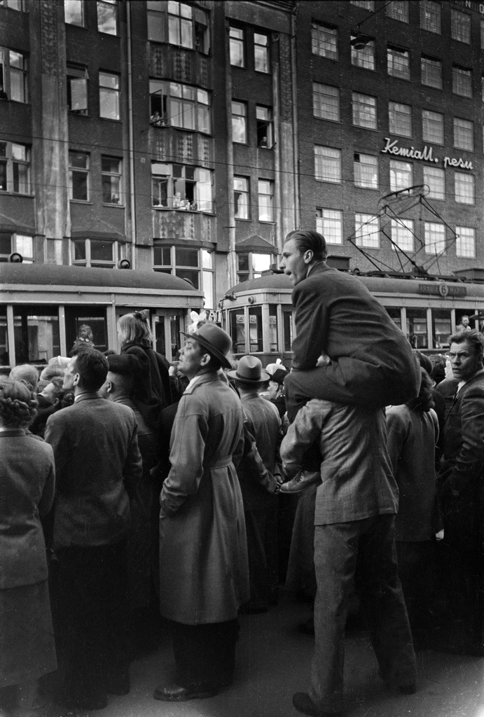 Helsingin 400-vuotisjuhlat. Yleisöä katsomassa Helsingin historiaa esittelevää juhlakulkuetta Siltasaarenkadun varrella, vastapäätä Siltasaarenkatu 3 - 1. Yksi mies toisen olkapäillä. Kadulla raitiovaunu numero 6.