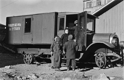 Elannon päiväkodin lapsia leikkimässä Viides linja 4:n pihalla olevan vanhan auton luona. Auto on käytöstä poistettu leipäauto ja siitä on tehty lasten leikkipaikka. Sen kyljessä lukee "poikien ikioma ja tyttöjen".  similar photo