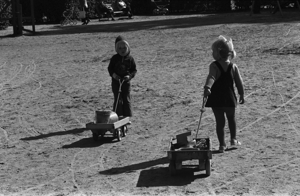 Tehtaanpuisto. Kaksi lasta vetämässä perässään pikkukärryjä Tehtaanpuiston leikkipaikalla.