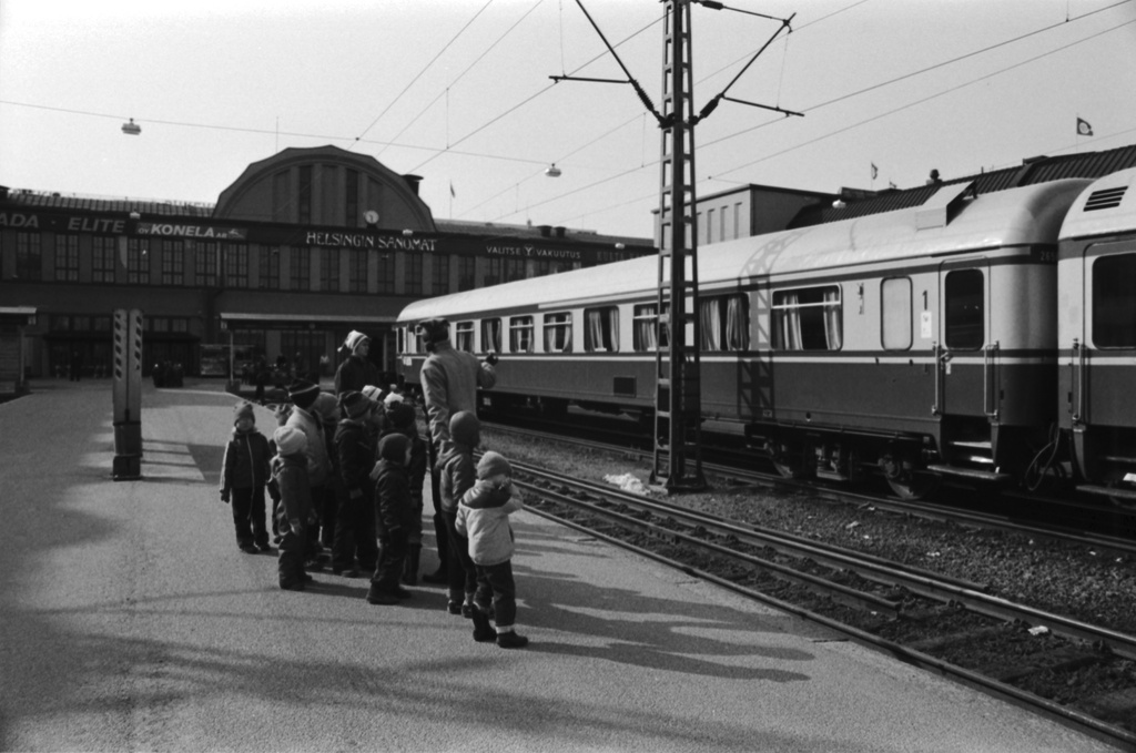 Kaivokatu 1. Vironniemen päiväkodin lapsia ja aikuisia asemalaiturilla katsomassa junia tutustumiskäynnillään Helsingin rautatieasemaan. Näkymä etelään.