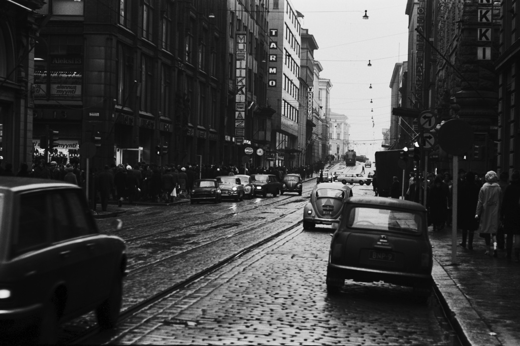 Kluuvi, Aleksanterinkatu. Jalankulkijoita ja ajoneuvoliikennettä sumuisella Aleksanterinkadulla puolen päivän aikaan. Mikonkadun risteyksen liikennevaloihin on pysähtynyt autokoulun auto. Näkymä Senaatintorin suuntaan.