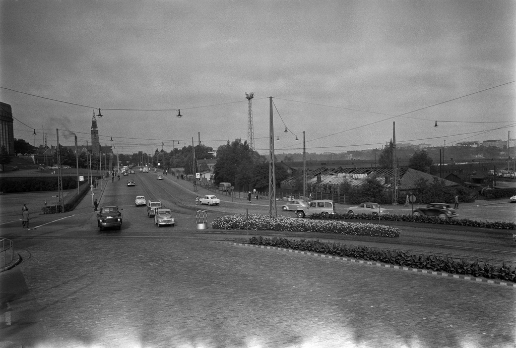 Liikennettä Mannerheimintien ja Arkadiankadun risteyksessä. Taustalla oikealla purkutyö Töölön tavara-aseman ratapihalla.