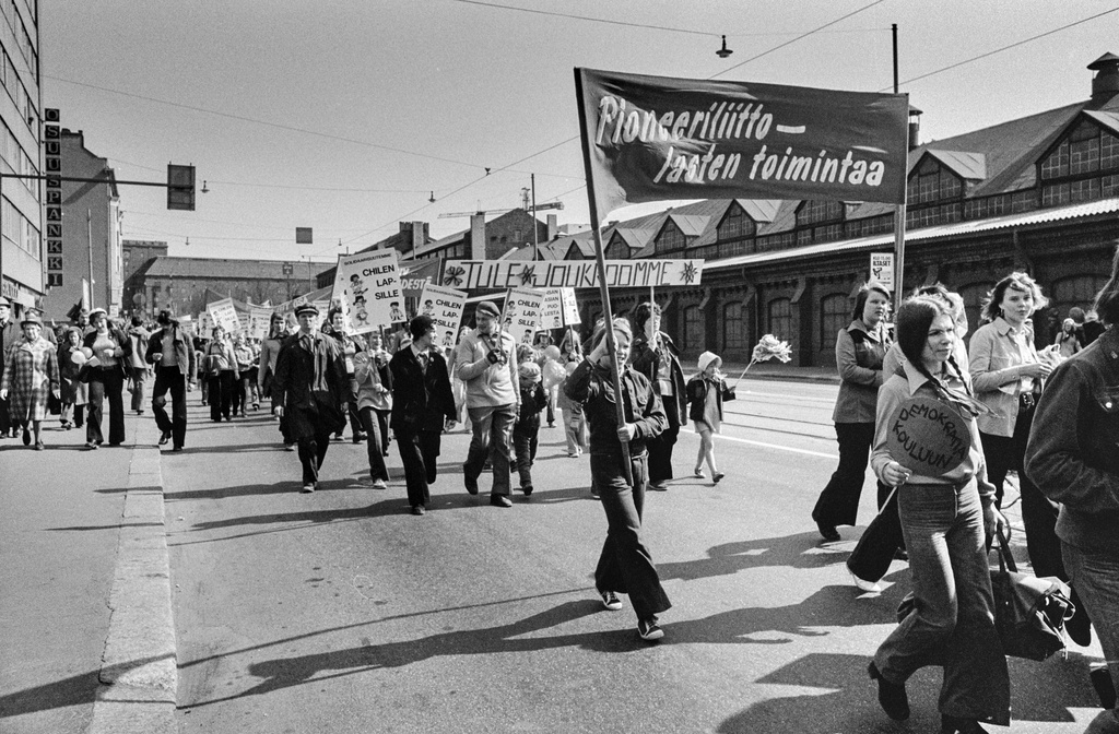 Vappumarssijoita Hämeentiellä. Edessä nuoret kantavat banderollia, jossa teksti: Pioneerilliitto - lasten toimintaa. Takana banderolli, jossa teksti: Tule joukkoomme ja kylttejä, joissa teksti: Solidaarisuutemme Chilen lapsille.