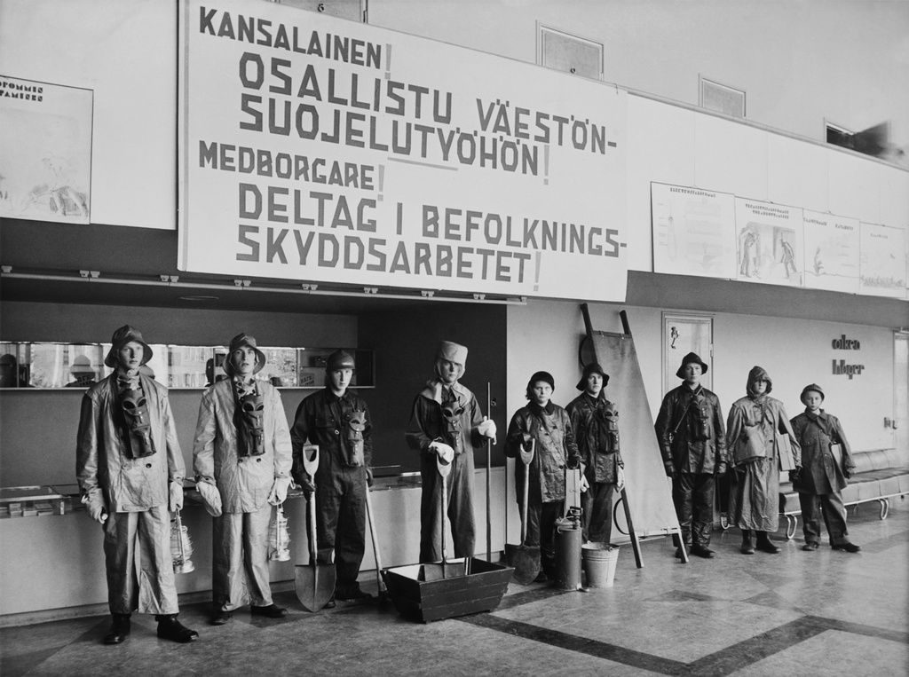 Suojavarustein ja apuvälinein varustautuneita koulupoikia rivissä seisomassa Bio Rexin aulatiloissa. Kyseessä mahdollisesti SKJ:n (Suomen kaasusuojelujärjestö) järjestämät väestönsuojelun neuvonta- ja opastuspäivät syyskuun lopussa 1939.