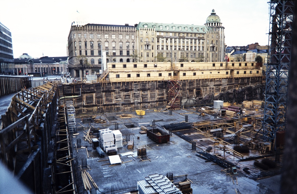 Forumin kauppakeskuksen perustuksen rakentamisvaihe, Mannerheimintie 20 - Simonkatu 2. Työmaakoppien rivistö Mannerheimintien suuntaisesti  Takana Mannerheimintie 3, 5, 7.