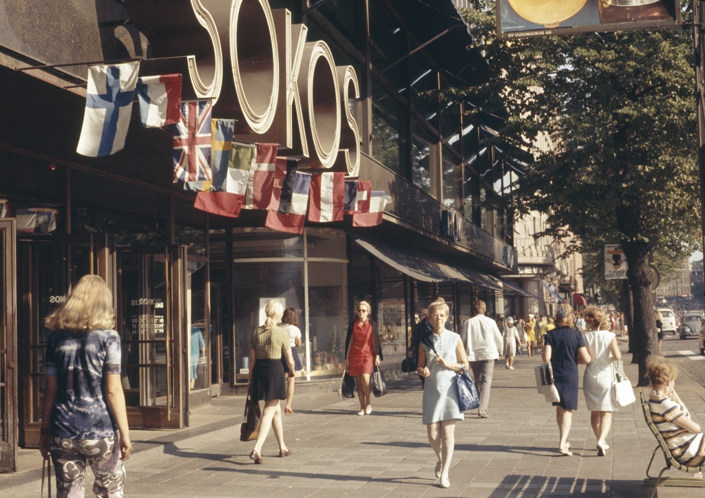 Jalankulkijoita Mannerheimintiellä Sokoksen tavaratalon kohdalla. Eri maiden lippuja. Mannerheimintie 9.