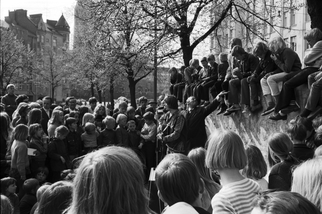 Karhupuisto. Helsingin juhlaviikot. Jukka Kuoppamäki lavalla aloittamassa esiintymistä runsaslukuiselle yleisölle Karhupuistossa järjestetyssä puistotapahtumassa. Lavalla myös puistojen mies.