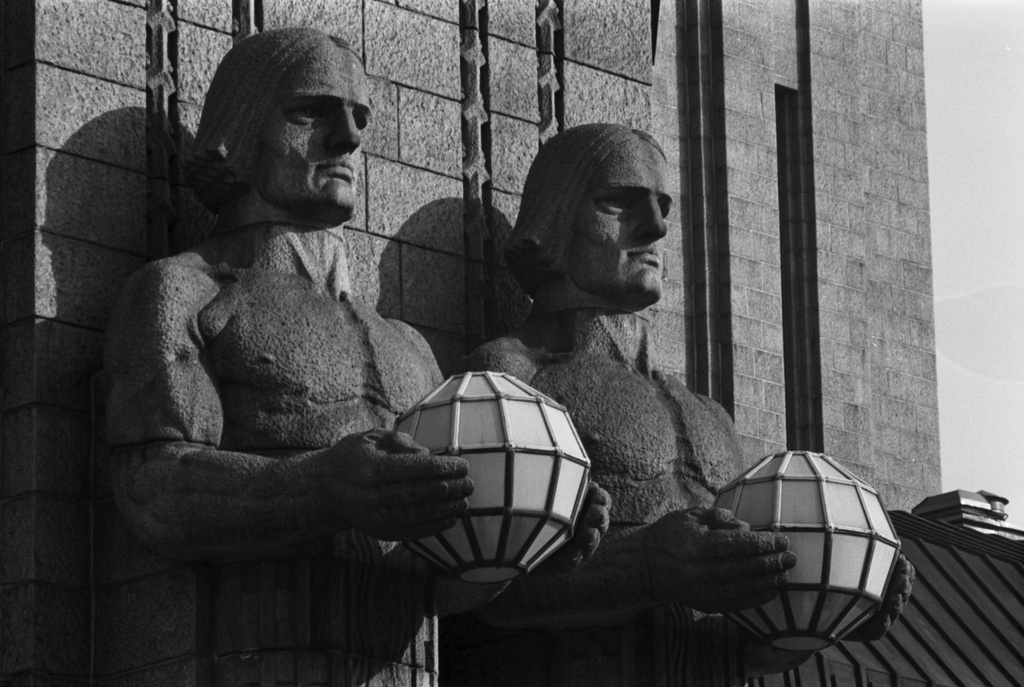 Kaivokatu 1. Kuvanveistäjä Emil Wikströmin veistämät graniittiset Lyhdynkantajat-hahmot Helsingin rautatieaseman pääsisäänkäynnin oikealla puolella.