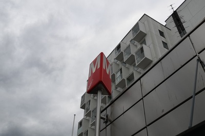 Rastilan metroasema Vuosaaressa. Metroaseman merkki lähikuvassa. Takana asuinrakennus. rephoto