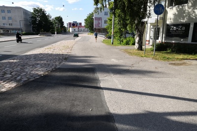 Malmi Ylä-Malmi. Kolme naista, todennäköisesti postinjakajia, polkupyörineen Kirkonkyläntiellä. Syksyinen näkymä auton ikkunasta. Oikella talo, jossa ravintola Malmi Kesti ja R-kioski. Kioskin luukulla mies asiomassa. rephoto