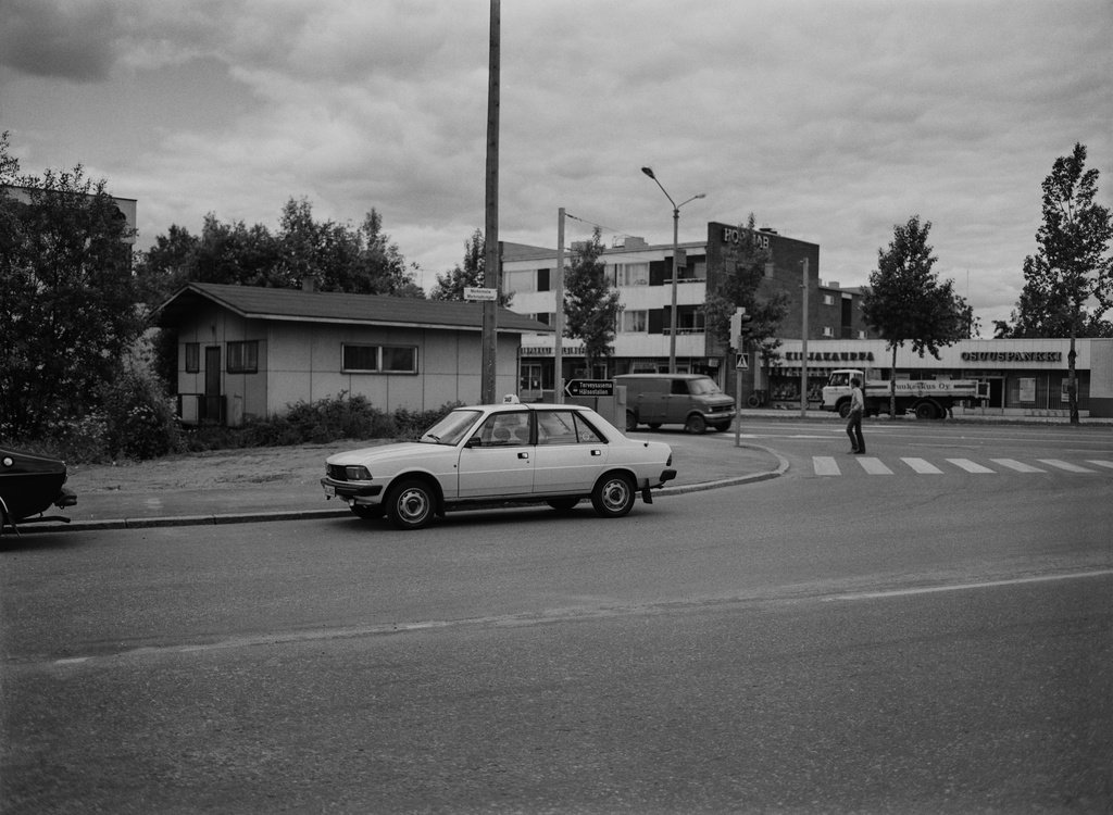 Ylä-Malmi. Markkinatie1 - Kirkonkyläntie 10. Taustalla Helsingin osakepankki, kirjakauppa ja Osuuspankki Kirkonkyläntie 11:ssä ja 13:ssa. Markkinatielle pysäköity valkoinen taksi on Peugeot 305.