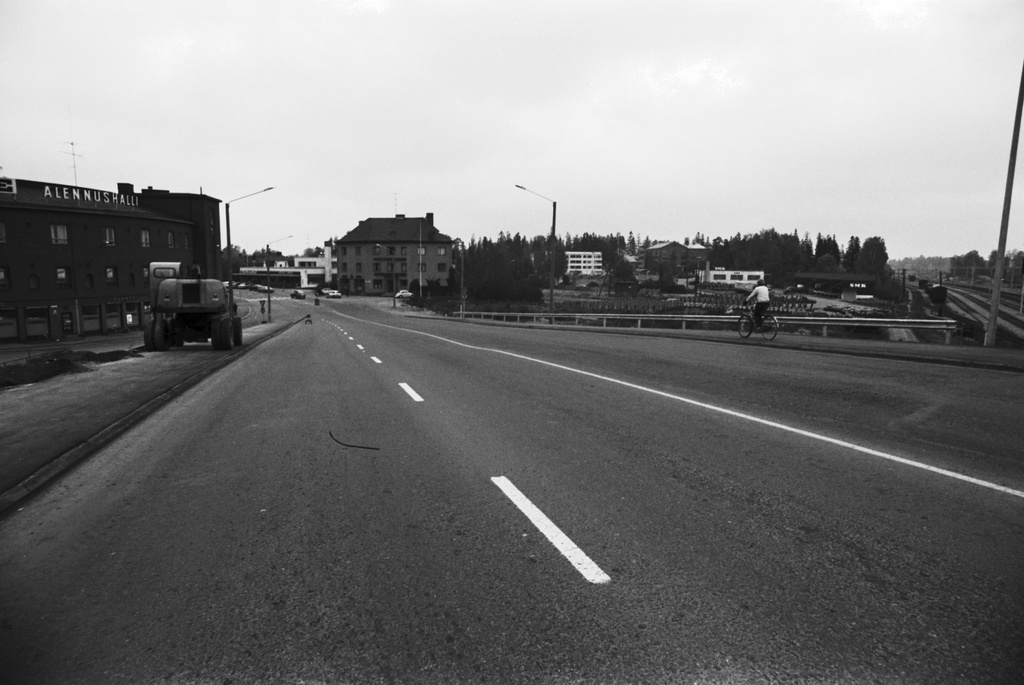 Malmi, Ylä-Malmi, Kirkonkyläntie. Näkymä pääradan ylittävältä maantiesillalta Kirkonkyläntien alkupäästä pohjoiseen, Ylä-Malmin suuntaan. Vasemmalla Malmin Elannon rakennuksessa  E-Alennushalli. Oikealla Suomen Maanviljelijäin Kauppa SMK:n myyntikonttori ja varasto paikalla, jossa nykyisin on Malmin kauppakeskus ja Ylä-Malmin tori.