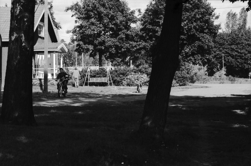 Viikinkaari 8. Näkymä Viikin Latokartanosta vanhan puutalon pihapiiristä. Vasemmalla mopoa ajava mies, todennäköisesti postinjakaja.