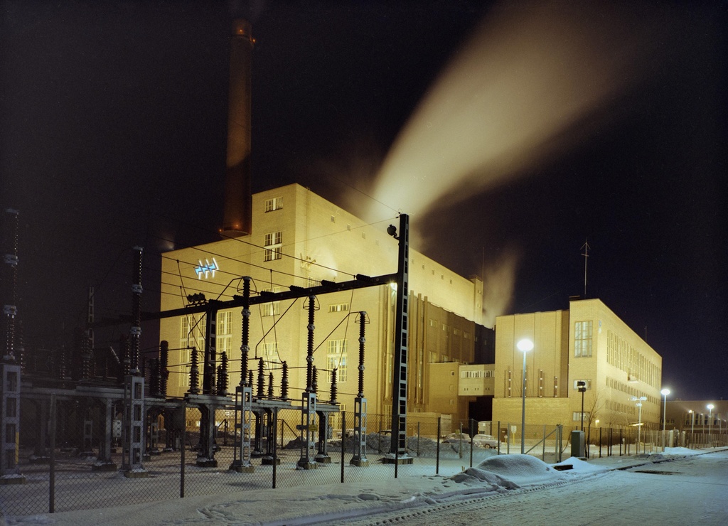 Salmisaaren voimalaitos iltavalaistuksessa kuvattuna Pikku-Pässin kujalta. Höyrypäästö varo- tai käynnistysventtiilin kautta.