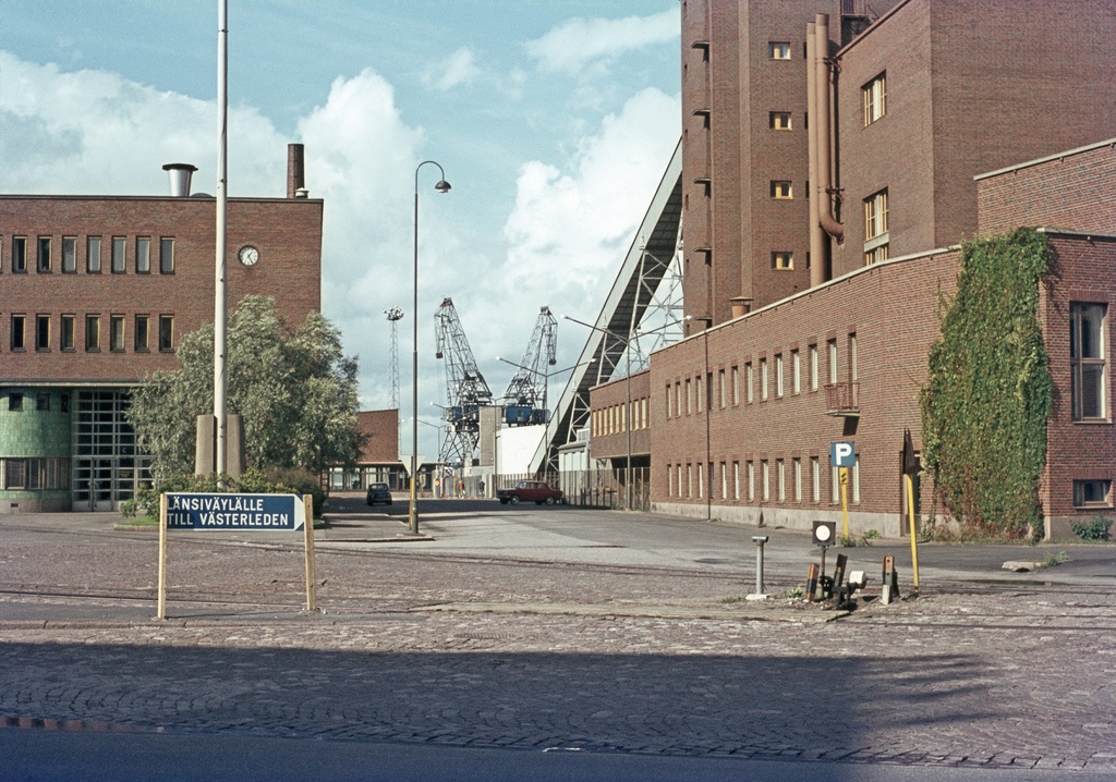 Vasemmalla Oy Alkoholiliike Ab:n (nyk. Oy Alko Ab) tehdas (nyk. Helsingin oikeustalo, Salmisaarentalo), Itämerenkatu 51 (nyk. Porkkalankatu 13). Oikealla Helsingin kaupungin sähkölaitoksen (nyk. Helsingin Energia) Salmisaaren voimala, Lauttasaarenkatu 11 (=Porkkalankatu 11). Keskellä Tallberginkatu.